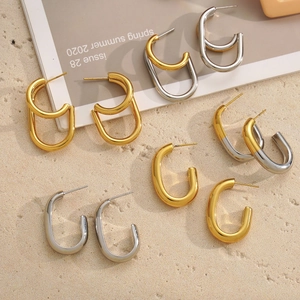 Minimalist C-shaped geometric hoop earrings in gold and silver finish on sand background