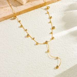 Close-up of gold Y-shaped necklace with crystal bezel charms on textured stone