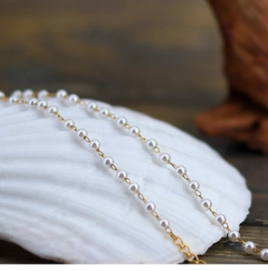 Macro detail of elegant mini white pearls on a fine gold chain over a shell