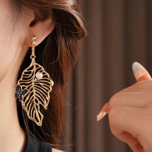 Detail of golden hollow leaf earrings with white pearl and black butterfly accent