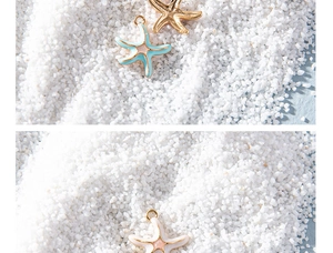 Close-up of alloy starfish charms with blue and white enamel on white sand background