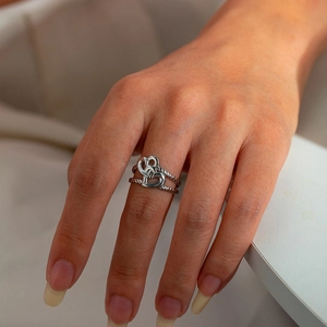 Detail of silver stainless steel ring with heart and knot design worn on hand