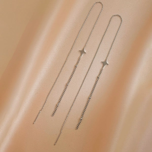 Macro shot of silver star tassel earrings draped on elegant champagne silk fabric