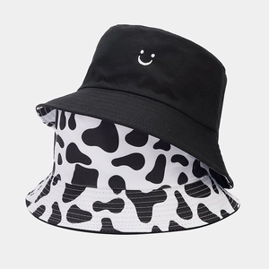 Close-up of reversible bucket hat featuring cow print and black embroidered smiley face