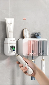 Detail of wall-mounted toothpaste dispenser and two cups on grey marble tile