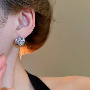 Close-up of diamond-encrusted clover earring with pink gemstones on a model ear