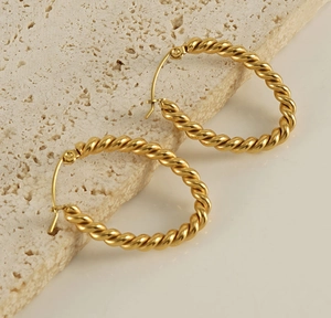 Close-up of golden twist hoop earrings with spiral texture on a beige stone surface