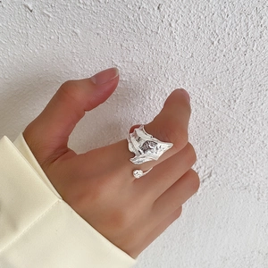 Close-up of irregular textured silver ring worn on model hand against minimalist wall