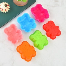 Top view of six colorful bear-shaped silicone baking molds on white marble surface