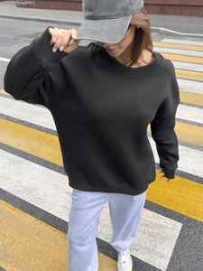 Outdoor street shot of women's black crewneck sweatshirt with ribbed cuffs and hem