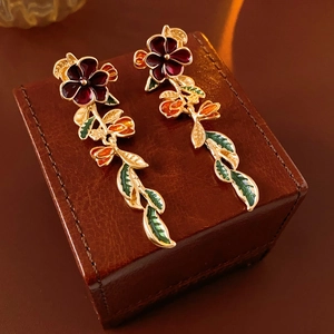 Detail von roten Blumenohrringen mit goldgeränderten grünen Blättern auf Lederbox