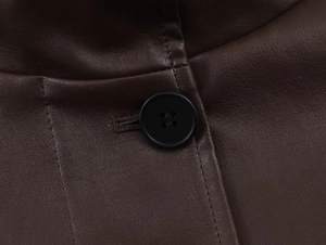 Macro shot of dark brown faux leather texture with black four-hole button and stitching