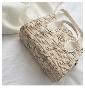 Detail view of woven straw bag bottom with floral embroidery and cream leather handle