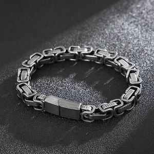 Gros plan d'un bracelet byzantin en argent au style industriel sur fond noir mat