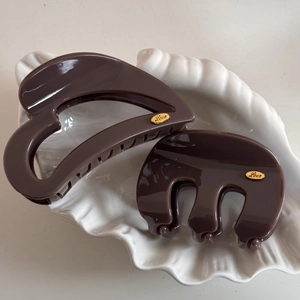Detailed view of dark brown hair claws with gold Love emblem in a shell dish
