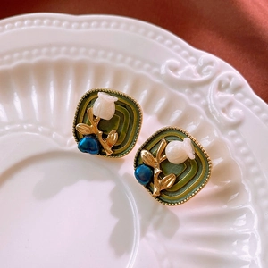 Macro shot of vintage square gold-rimmed earrings with white floral and blue bead details
