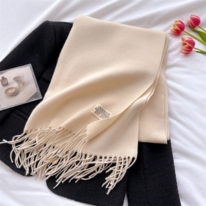 Detailed shot of beige cashmere-feel scarf with tassels folded on a textured black coat