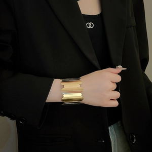 Close-up of a wide golden cuff bracelet with wavy edges on a black suit background