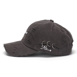 Close-up of distressed black cotton cap with silver metal rings and letter embroidery