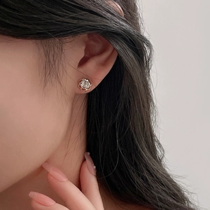 Close-up of rose gold hollow flower earring with a bright zircon stone on an ear lobe
