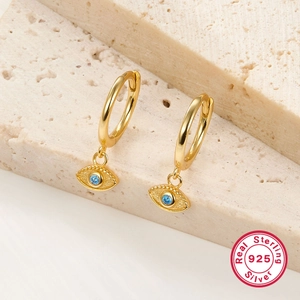 Macro view of gold S925 sterling silver hoop earrings with blue eye charms on stone
