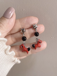 Detail of red enamel pony earrings with silver star and black bead on hand