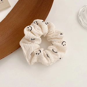 Detail view of a cream-colored waffle fabric scrunchie with black smiley face patterns
