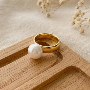 Top view of an elegant gold stainless steel ring with a pearl on a wooden tray