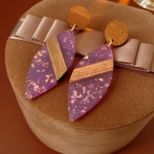 Détail de boucles d'oreilles en bois et résine violette avec feuilles d'or