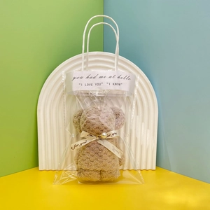 Close-up of khaki coral fleece bear-shaped towel gift in transparent bag with pearl detail