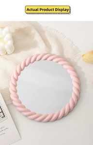 Pink round makeup mirror with cream-style twisted frame on a white textured background