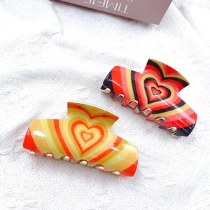 Cute heart pattern acrylic hair claw clips in yellow and red on white textured fabric