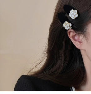 Detail of two white pearl camellia hair clips worn on side of brown hair for elegant styling