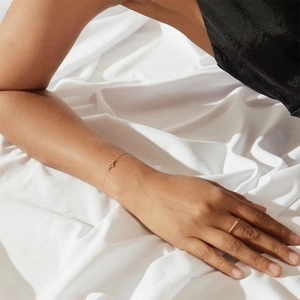Close-up of a minimalist gold snake charm bracelet and ring set on white fabric