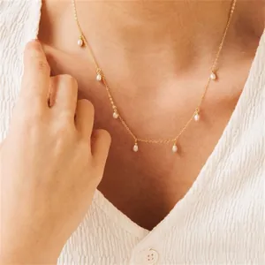 Close-up of gold chain necklace with white teardrop pearls worn on a model collarbone