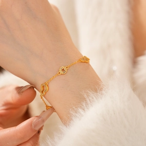 Close-up of 24k gold-plated bracelet featuring heart and coin charms with zircon stones