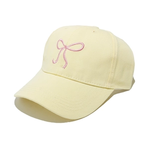 Detailed macro view of cream baseball cap featuring pink embroidered bow and stitching