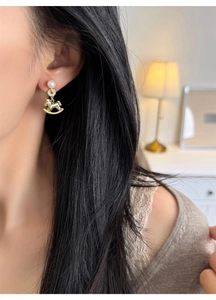 Close-up of golden rocking horse earrings with pearls worn by a model in soft light