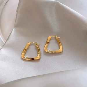 Detailed close-up of golden twisted geometric hoop earrings on elegant silk background