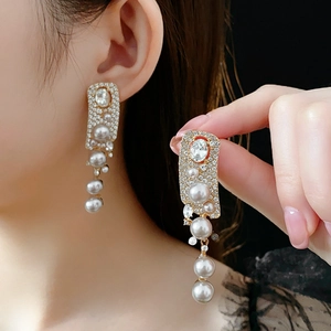 Close-up of elegant gold dangle earrings with large oval rhinestones and white pearls