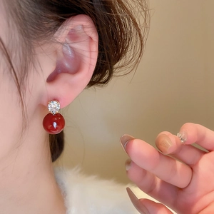 Detail of elegant gold-plated stud earring with sparkling zircon and glossy red pearl