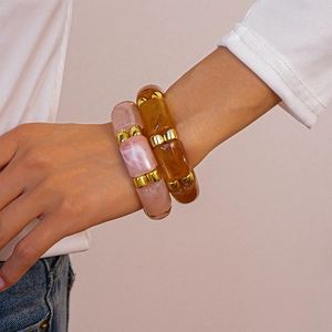 Detail of amber and peach acrylic geometric bracelets with gold beads on a model