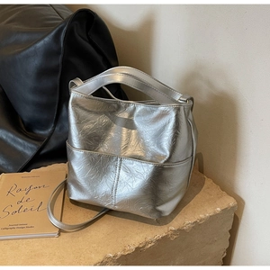 Silver bucket bag detail featuring pleated metallic texture on a stone pedestal
