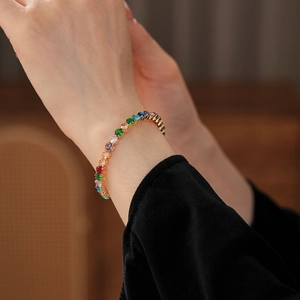 Close-up of a gold tennis bracelet featuring multi-colored zircons on a model wrist