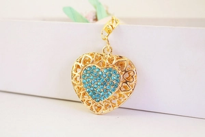 Detail of a golden heart keychain with light blue rhinestones on a white surface