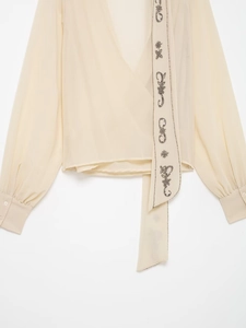 Detailed close-up of beige chiffon blouse featuring beaded ribbon with rhinestone moon and stars