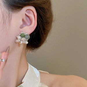 Detailed view of elegant silver flower earrings with green beads and white pearls on a model