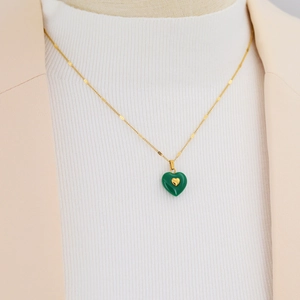 Elegant gold chain necklace featuring a green heart pendant worn with a white knit sweater