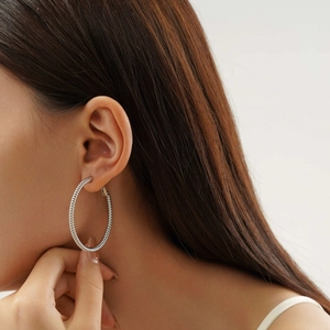 Detail of silver twisted spiral hoop earrings worn by a model in a close-up shot