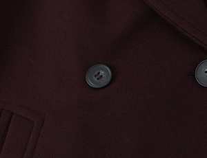 Close-up detail of burgundy wool coat fabric and dark grey resin buttons texture